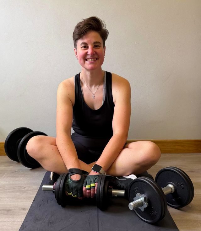 Sandra, sentada en el suelo con dos mancuernas, sonriendo a cámara